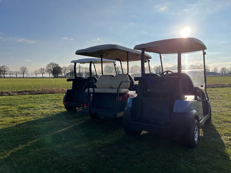 Twee golfkarren van Greengolfcarts in het veld bij laagstaande zon