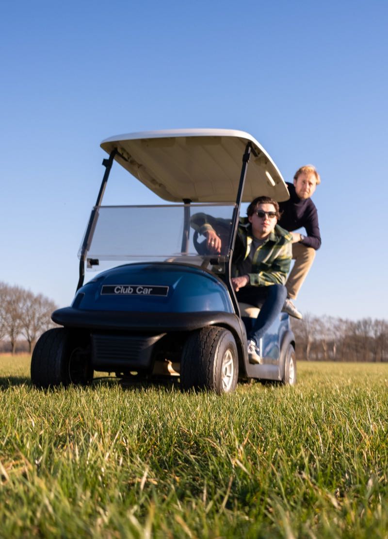 Twee mensen rijden in een blauwe Club Car-golfkar over het gras